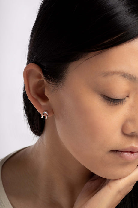 Boucles d'oreilles Maison Mouche au design épuré et architectural, en argent 100% recyclé et tracé, fabriquées dans des ateliers eco-responsables en Italie. Cette mini boucle L'AVENTURE enrobe discrètement l'oreille, elle est un jeu d’oppositions et de ruptures entre courbes et segments. Les biais accentuent les perspectives, la lumière avive les angles et découpe les espaces.